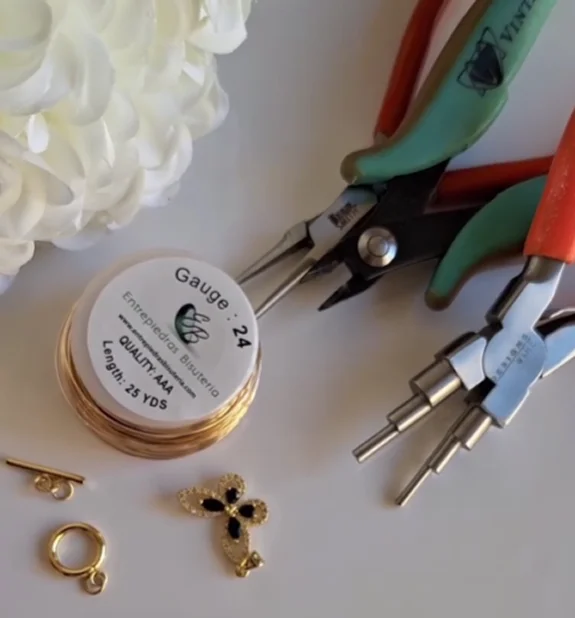 Un par de pendientes bañados en oro junto a unos alicates y una flor, que muestran una escena de fabricación de joyas.