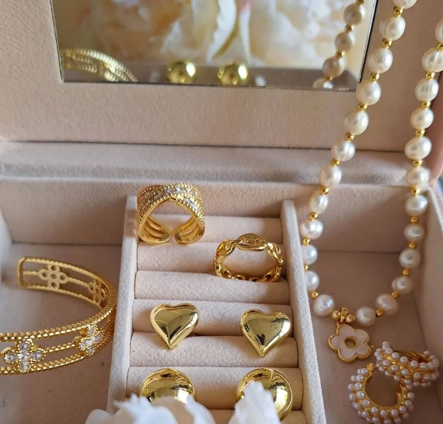 Caja abierta que contiene joyas de oro y perlas, destacando su brillo y elegancia en un fondo neutro.