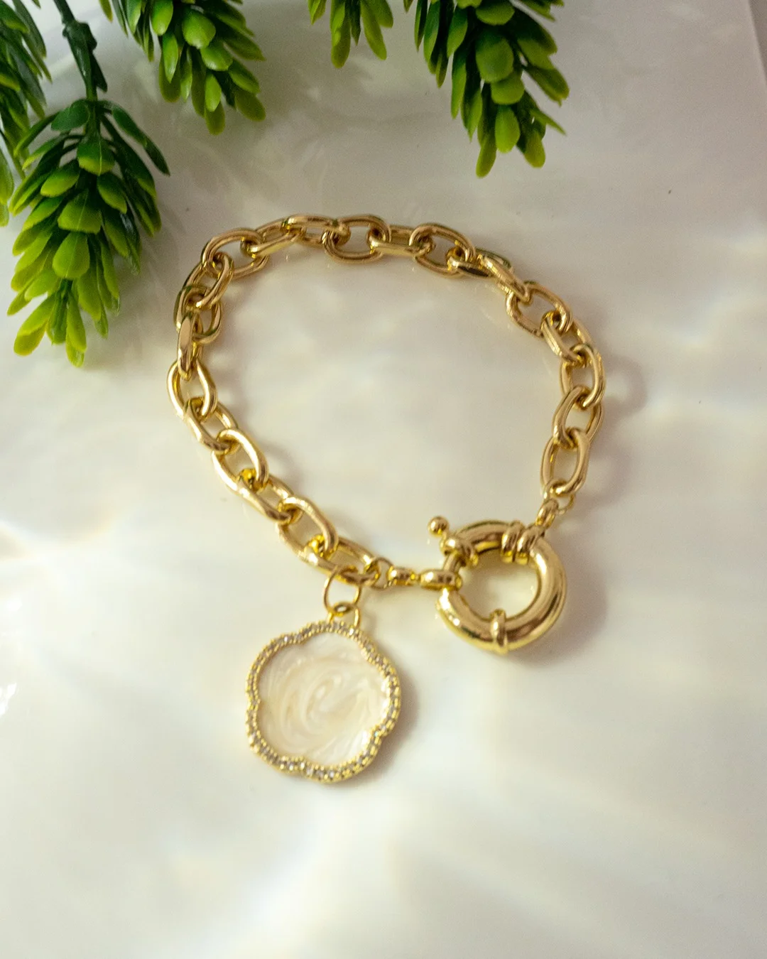 Pulsera de oro con un charm de moneda y una flor, destacando su diseño elegante y detalles delicados.