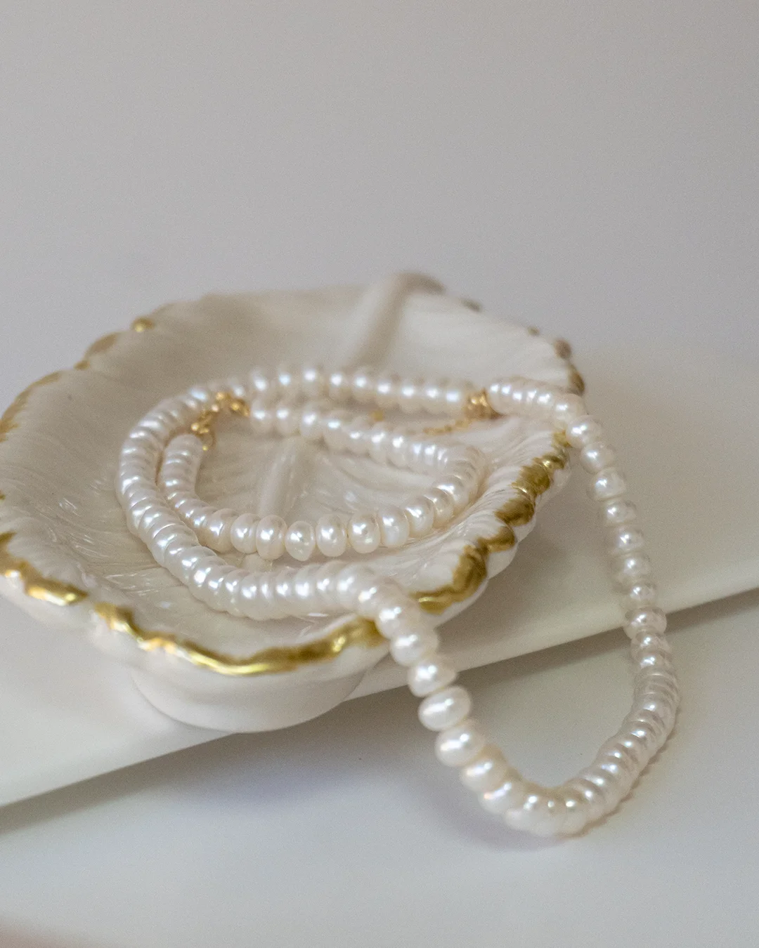 Collar de perlas blancas sobre un plato dorado, exhibiendo elegancia y sofisticación.