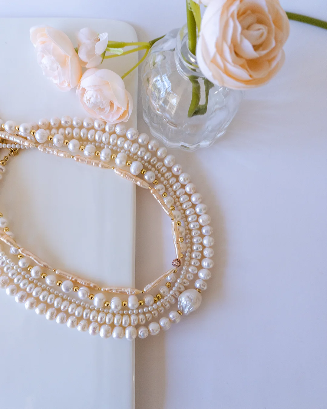 Collar de perlas y flores sobre una mesa blanca.